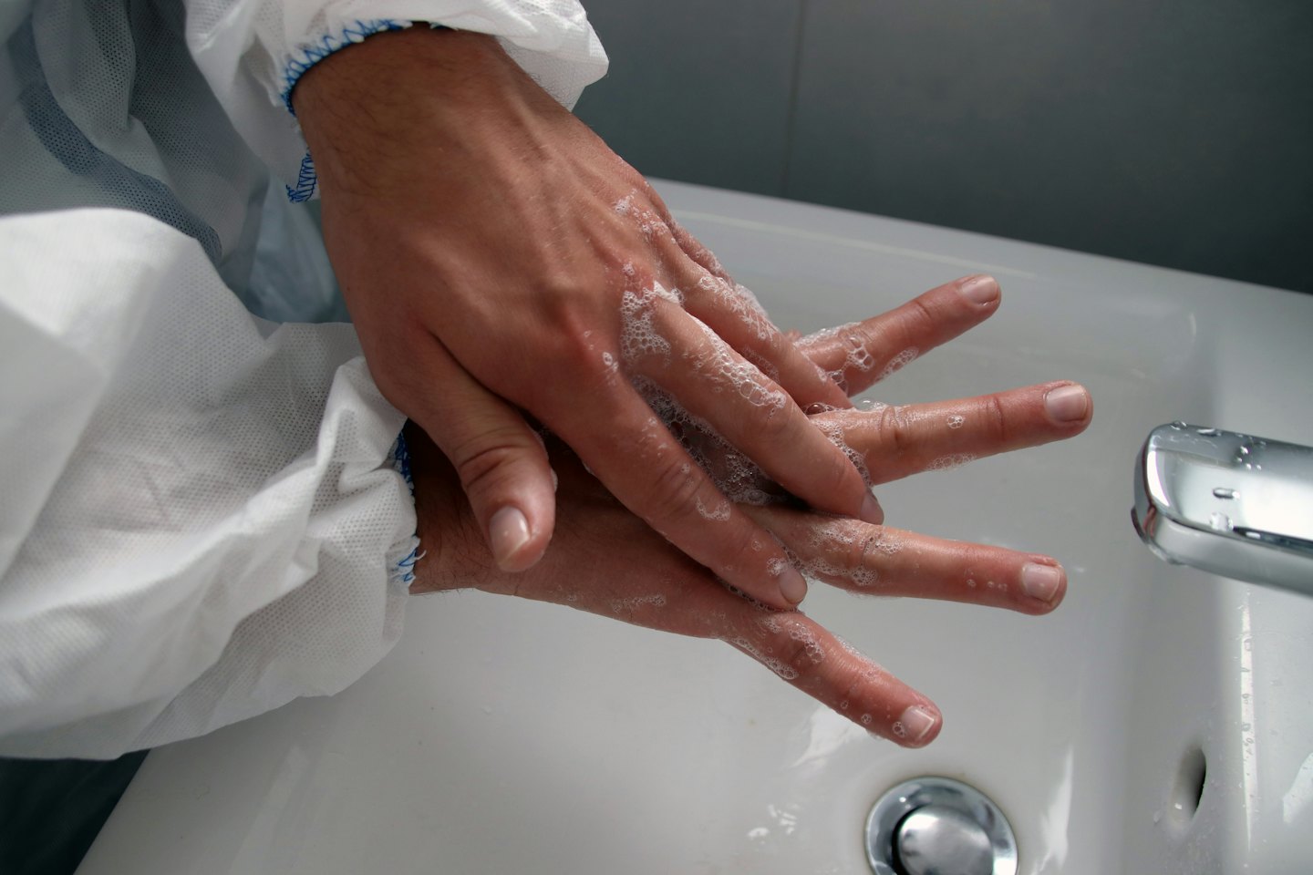 Hands covered in soap bubbles being washed in a sink.