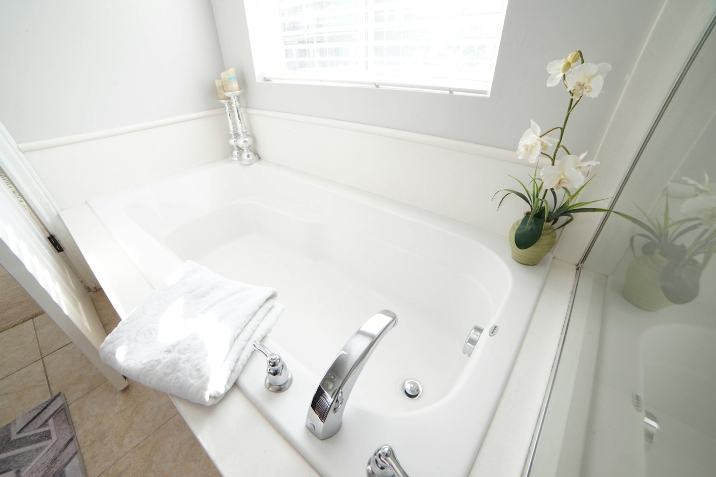Modern white bathtub with towel and orchid in bathroom.